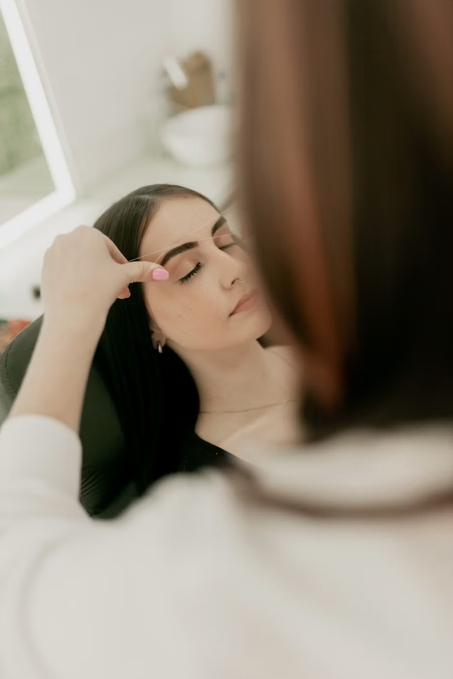 Una artista de cejas diseñando las cejas de una clienta en un estudio luminoso